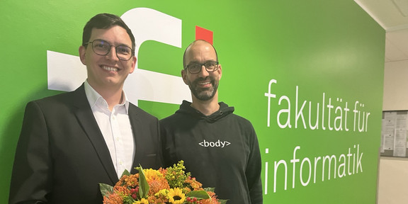 Sven Mayer and Mario Botsch in front of the computer science logo at TU Dortmund