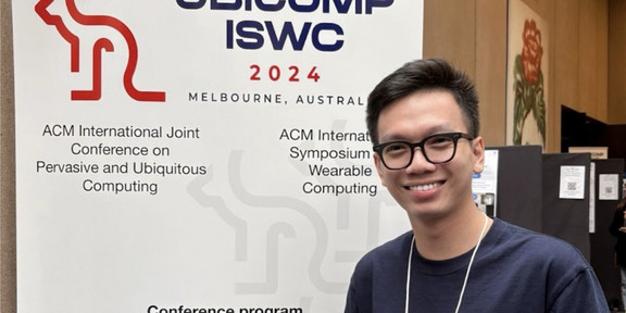 Toan in front of a UbiComp 2024 banner